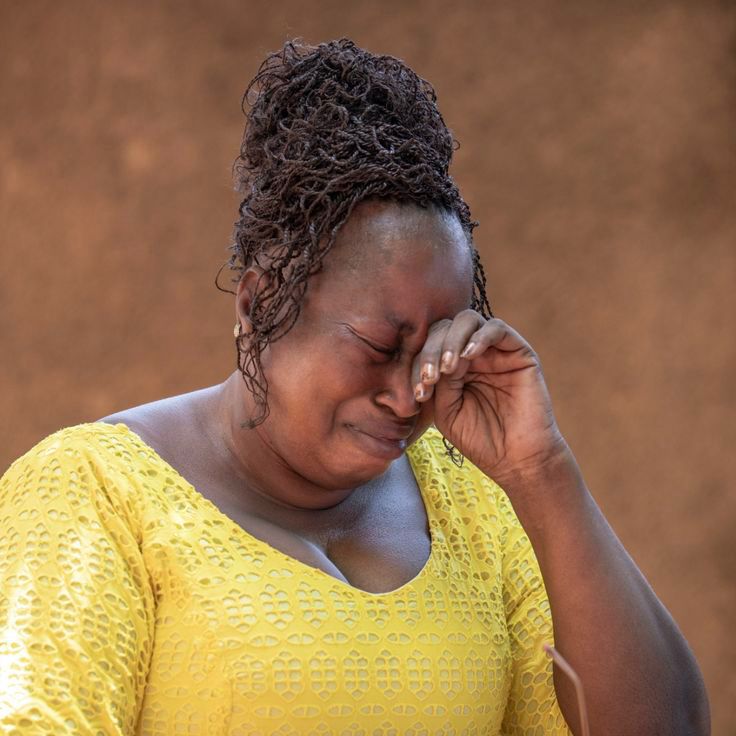A Ghanaian woman in a yellow dress wiping her eye in grief